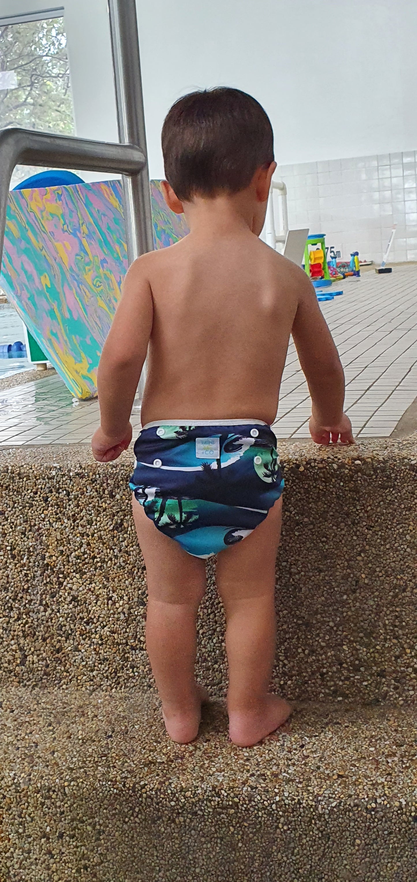 Eco-friendly swim nappy with a stylish palm tree pattern, made by Mini Me & Co, designed for a secure, leak-resistant fit from 4.5kg to 13.5kg.