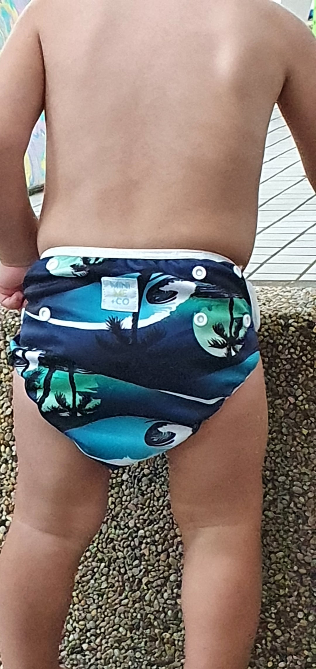 Eco-conscious palm tree-patterned reusable swim nappy by Mini Me & Co, designed with soft mesh lining and secure snaps for comfort and reliability.