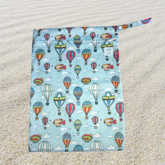 A colorful Hot Air Balloon Waterproof Wet Bag made from 100% PUL material. It measures 25cm (H) x 20cm (W) and features a durable zipper closure to securely contain wet items. The bag includes a handy latch for easy attachment to strollers or bags, making it perfect for transporting swimwear, dirty clothes, nappies, toiletries, and more. This reusable and eco-friendly wet bag offers a stylish storage solution for parents on the go.